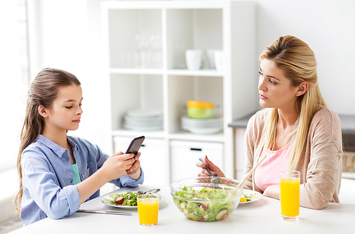 family, communication and people concept - sad mother looking at her daughter with smartphone having dinner at home