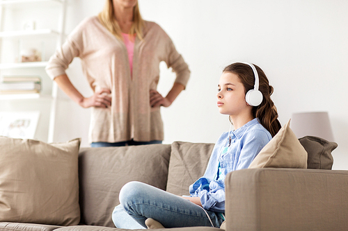 people, problem and family concept - girl with earphones sitting on sofa and angry mother at home