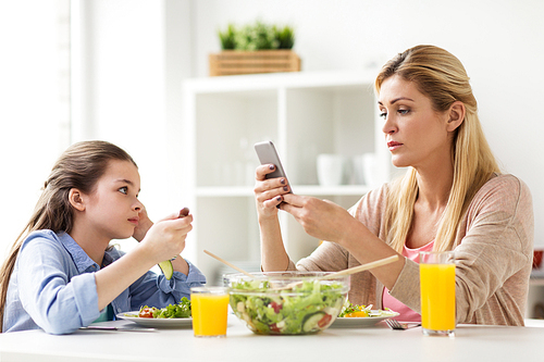 family, communication and people concept - sad girl looking at her mother with smartphone having dinner at home