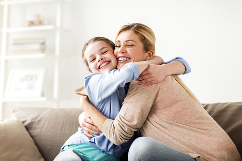 people and family concept - happy smiling girl with mother hugging on sofa at home
