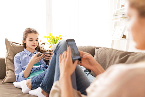 people, family and technology concept - happy girl and mother with smartphones at home