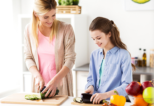 cooking food, healthy eating, family and people concept - happy mother and daughter chopping vegetables for dinner at home kitchen