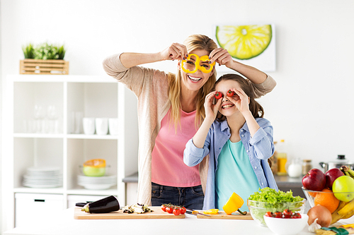 healthy eating, family and people concept - happy mother and daughter cooking vegetables for dinner and having fun at home kitchen