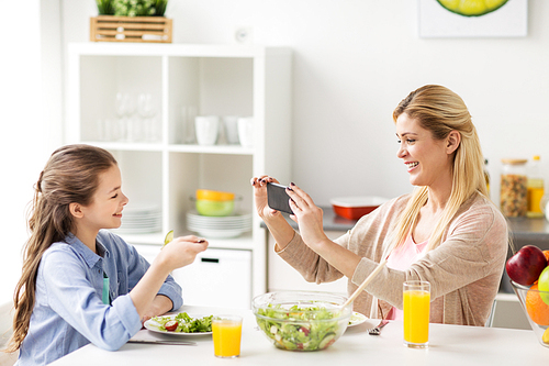 family and people concept - happy mother with smartphone having dinner and photographing her daughter at home kitchen