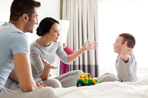 people and family concept - happy child with toy tractor and parents playing in bed at home or hotel room