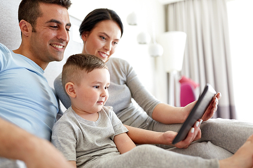 people, family and technology concept - happy mother, father and little boy with tablet pc computer in bed at home or hotel room
