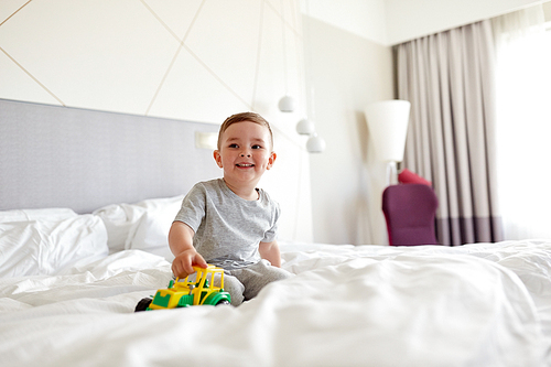 people, childhood and morning concept - happy little boy with toy car on home or hotel bed