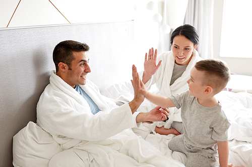 people, family and morning concept - happy child with parents in bed at home or hotel room