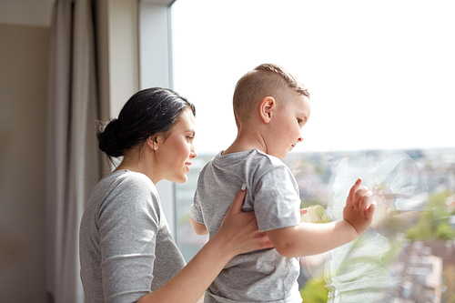 people and family concept - happy mother and little son looking through window at home