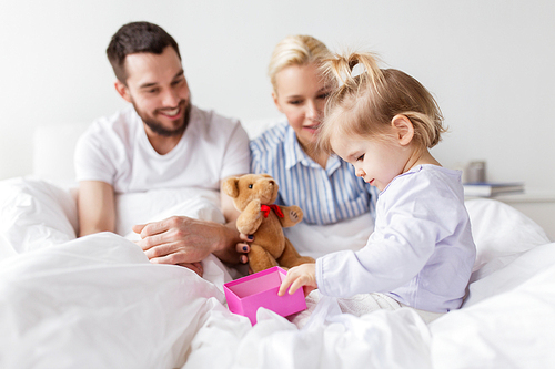 people, family, holidays and morning concept - happy little girl and parents with gift box in bed at home