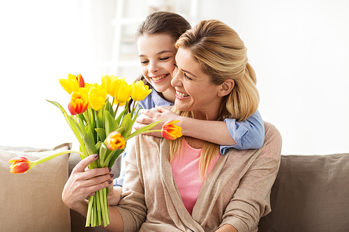 people, family and holidays concept - happy girl giving tulip flowers and hugging her mother at home