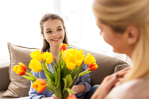 people, family and holidays concept - happy girl giving tulip flowers to her mother at home