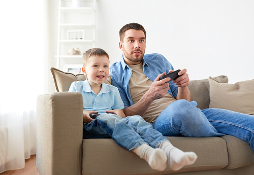 family, fatherhood and people concept - happy father and little son with gamepads playing video game at home