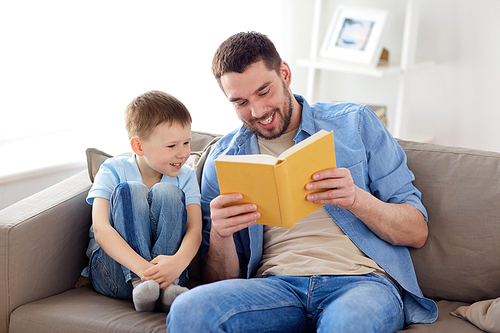 family, childhood, fatherhood, leisure and people concept - portrait of happy smiling father and little son reading book on sofa at home
