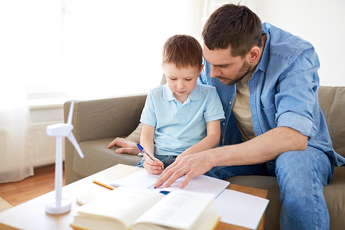 family, childhood, fatherhood and people concept - father and little with toy wind turbine drawing to notebook at home