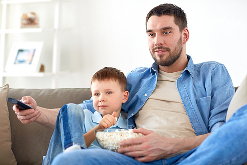 family, childhood, fatherhood, technology and people concept - happy father and little son with remote control and popcorn watching tv at home