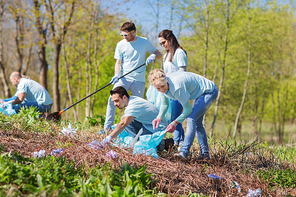 volunteering, charity, cleaning, people and ecology concept - group of happy volunteers with garbage bags cleaning area in park
