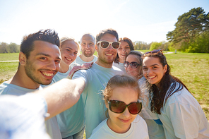 volunteering, charity and people concept - group of happy volunteers taking selfie by smartphone in park