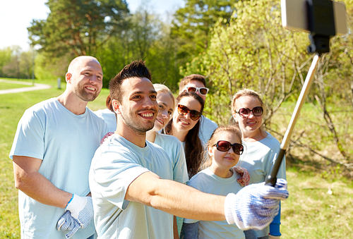 volunteering, charity and people concept - group of happy volunteers taking picture by smartphone and selfie stick in park