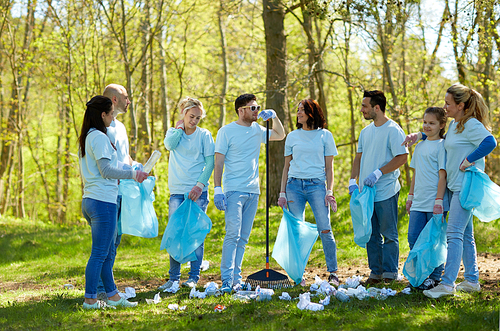 volunteering, charity, cleaning, people and ecology concept - group of happy volunteers with garbage bags and rake talking in park