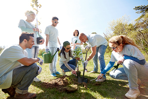 volunteering, charity, people and ecology concept - group of happy volunteers planting tree and digging hole with shovel in park