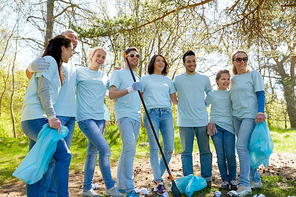 volunteering, charity, people and ecology concept - group of happy volunteers with garbage bags and rake cleaning area in park
