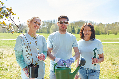 volunteering, charity, people and ecology concept - group of happy volunteers with tree seedlings and watering can in park