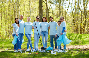 volunteering, charity, cleaning, people and ecology concept - group of happy volunteers with garbage bags and rake in park