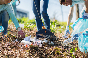 volunteering, people and ecology concept - group of happy volunteers with garbage bags and rack cleaning area in park