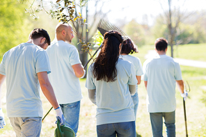 volunteering, charity, people and ecology concept - group of happy volunteers with tree seedlings and garden tools walking in park