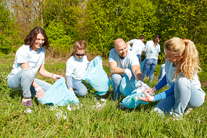 volunteering, charity, people and ecology concept - group of happy volunteers with garbage bags cleaning area in park