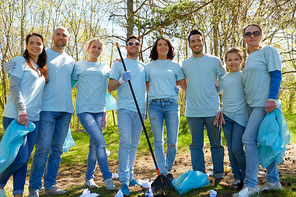 volunteering, charity, people and ecology concept - group of happy volunteers with garbage bags and rake cleaning area in park