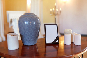 funeral and mourning concept - photo frame with black ribbon, cremation urn and candles on table in church