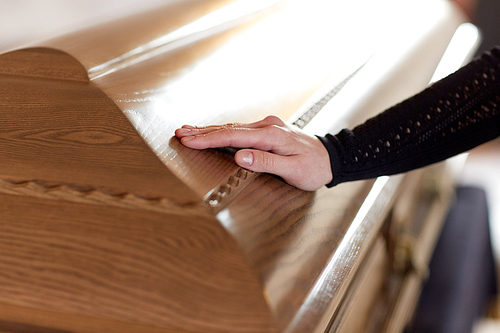 people and mourning concept - woman hand on coffin lid at funeral in church