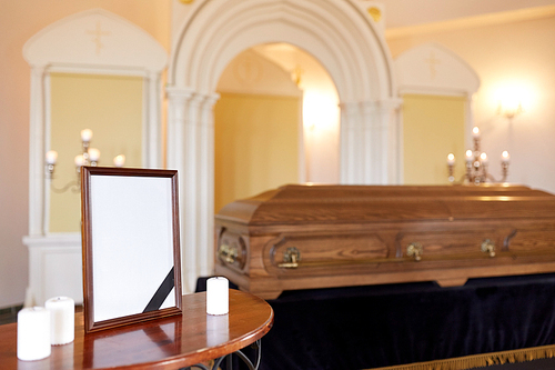 funeral and mourning concept - photo frame with black ribbon, candles and coffin at church
