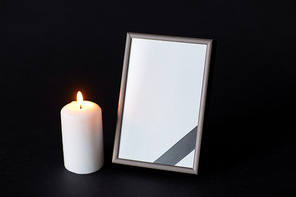 funeral and mourning concept - empty photo frame with ribbon and burning candle over black background