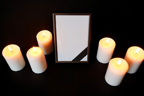 funeral and mourning concept - photo frame with black ribbon and burning candles over dark background
