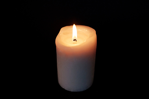 mourning and commemoration concept - candle burning in darkness over black background