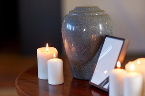 funeral and mourning concept - photo frame with black ribbon, cremation urn and burning candles on table in church