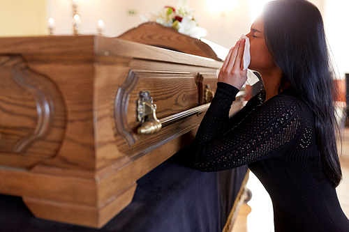 people and mourning concept - crying woman with coffin at funeral in church