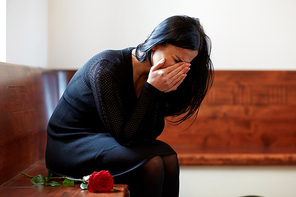 people, grief and mourning concept - crying woman with red rose sitting on bench at funeral in church