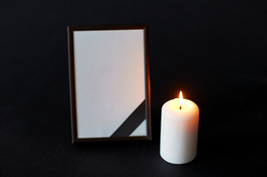 funeral and mourning concept - empty photo frame with ribbon and burning candle over black background