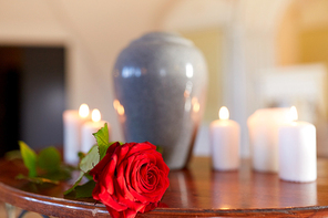 funeral and mourning concept - red rose and cremation urn with burning candles on table in church