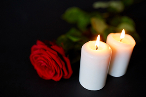 funeral and mourning concept - red rose and burning candles over black background