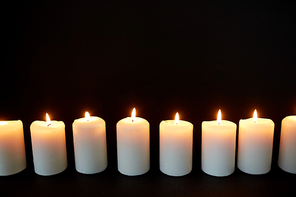 mourning and commemoration concept - candles burning in darkness over black background