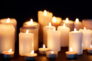 mourning and commemoration concept - candles burning in darkness over black background