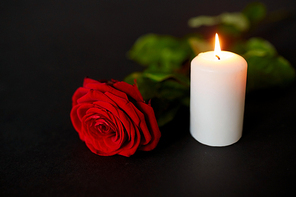 funeral and mourning concept - red rose and burning candle over black background