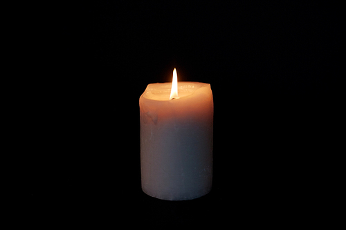 mourning and commemoration concept - candle burning in darkness over black background