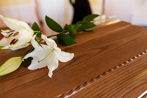 funeral and mourning concept - white lily flower on wooden coffin lid at funeral in church