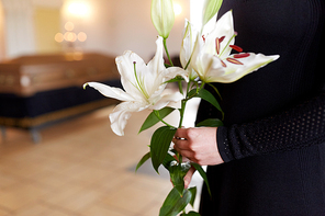 people and mourning concept - close up of woman with white lily flowers and coffin at funeral in church